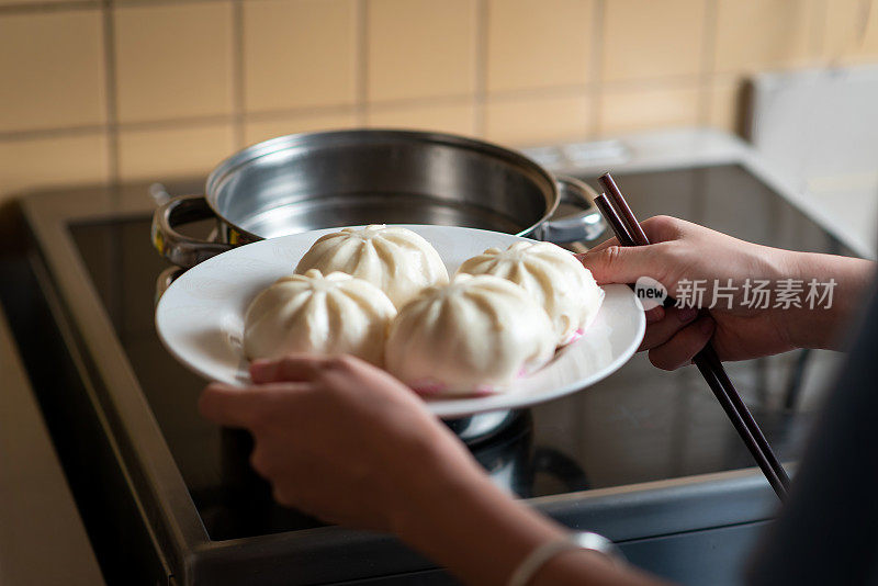 Woman taking out fresh baozi Chinese steamed buns from the metal steamer at home